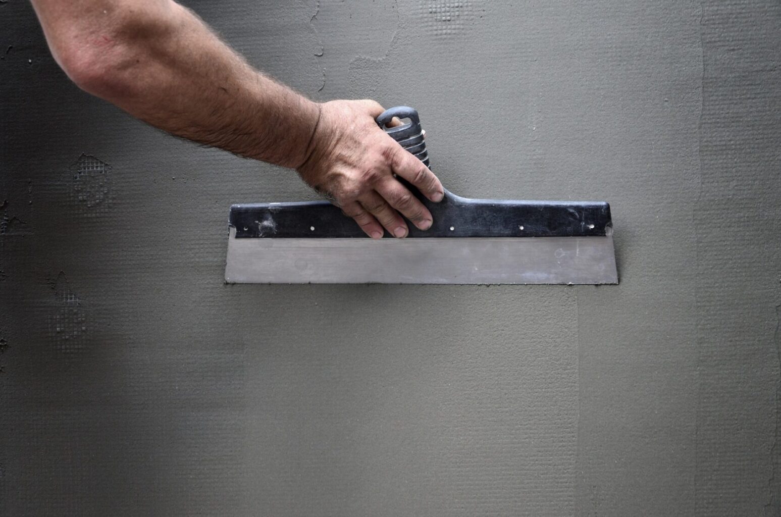 Hands of an old manual worker with wall plastering tools renovating house
